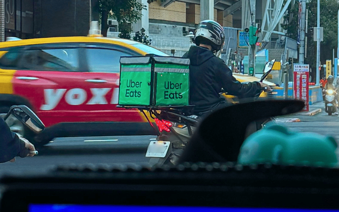 Uber Eats scooter courier carrying a green insulated delivery box through city traffic